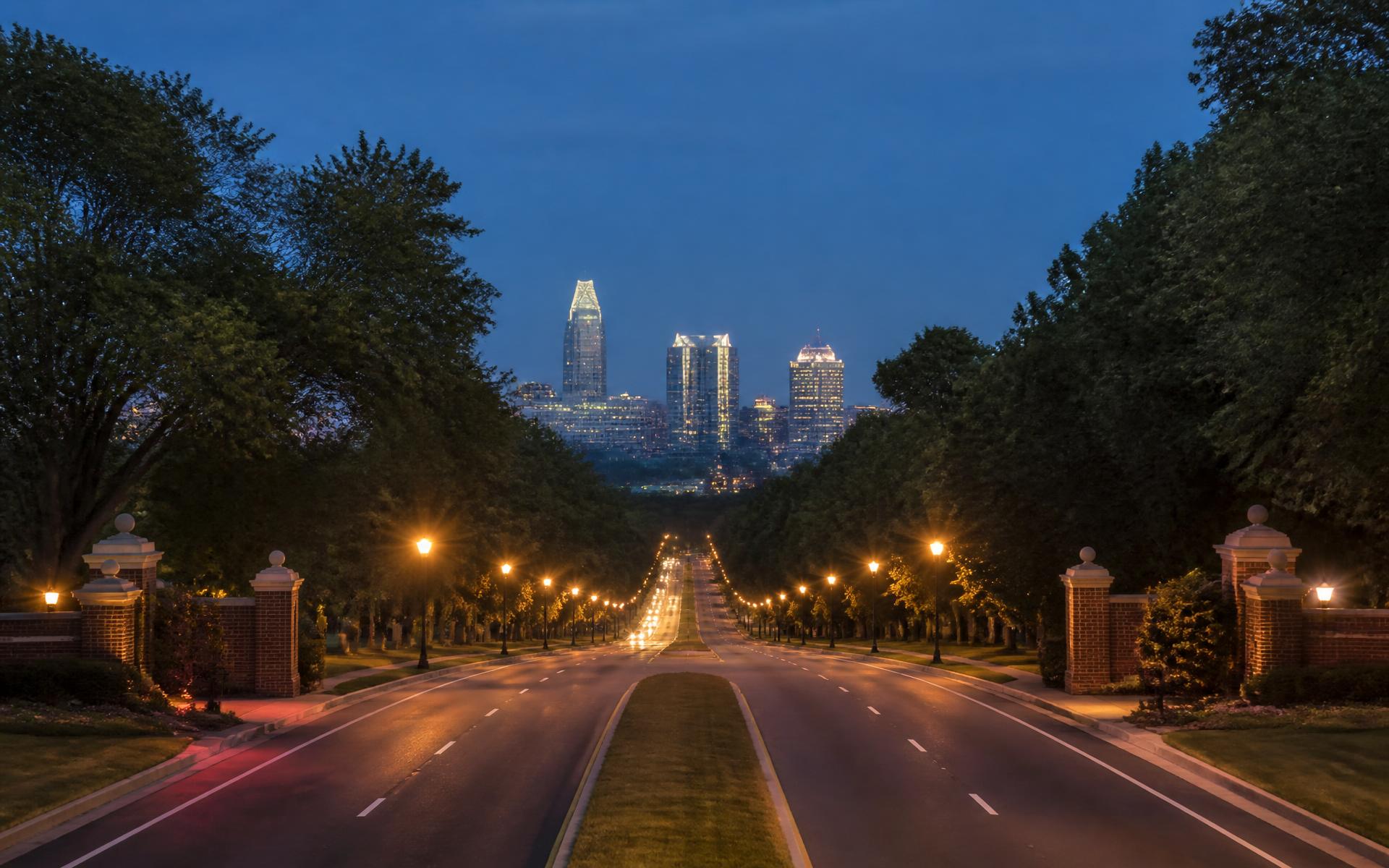 A tree-lined south Charlotte parkway at dusk with the Uptown Charlotte skyline in the distance